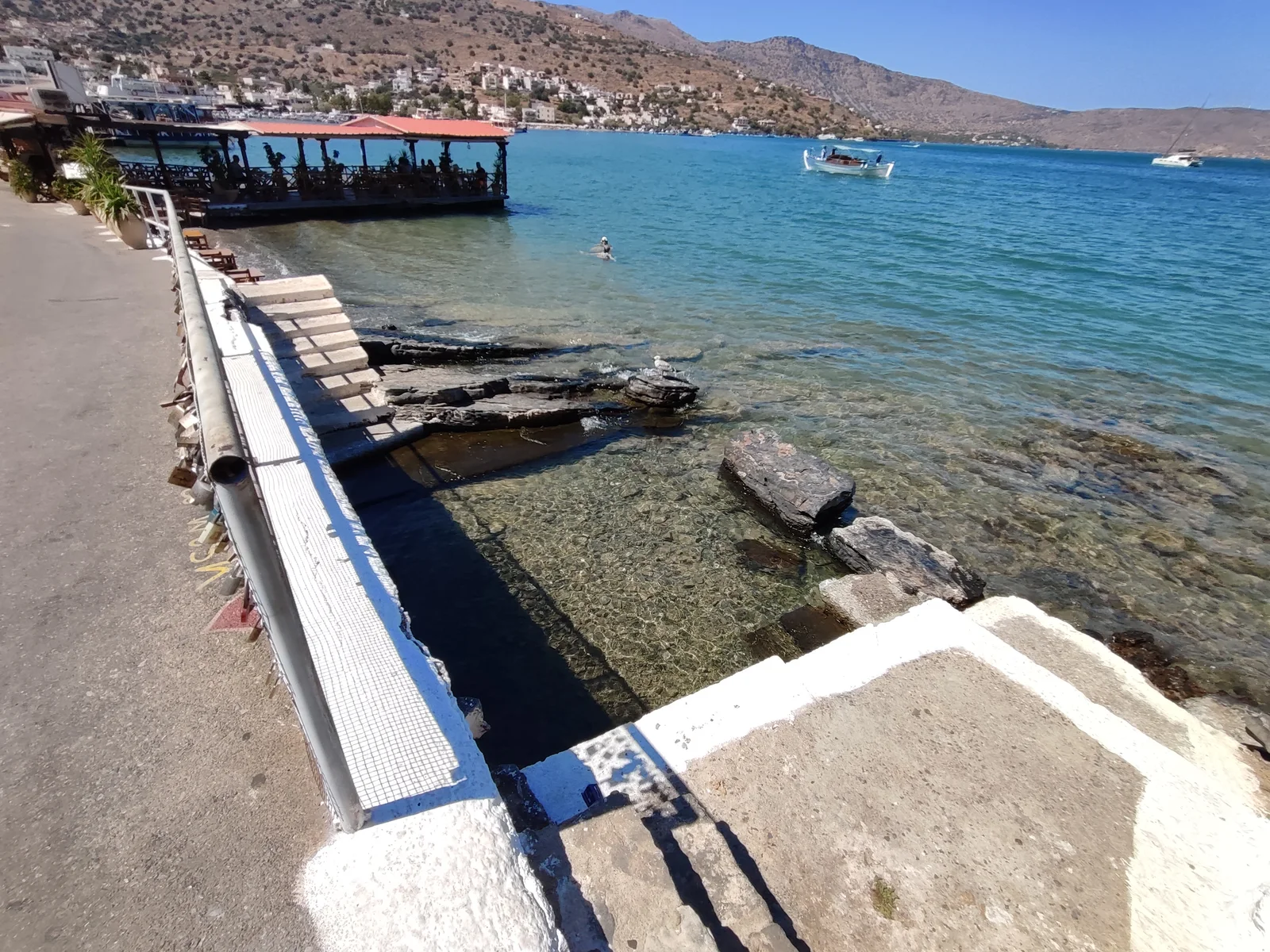 Stone-edged water beside the Schisma waterfront in Elounda, with the bay and lower village beyond.