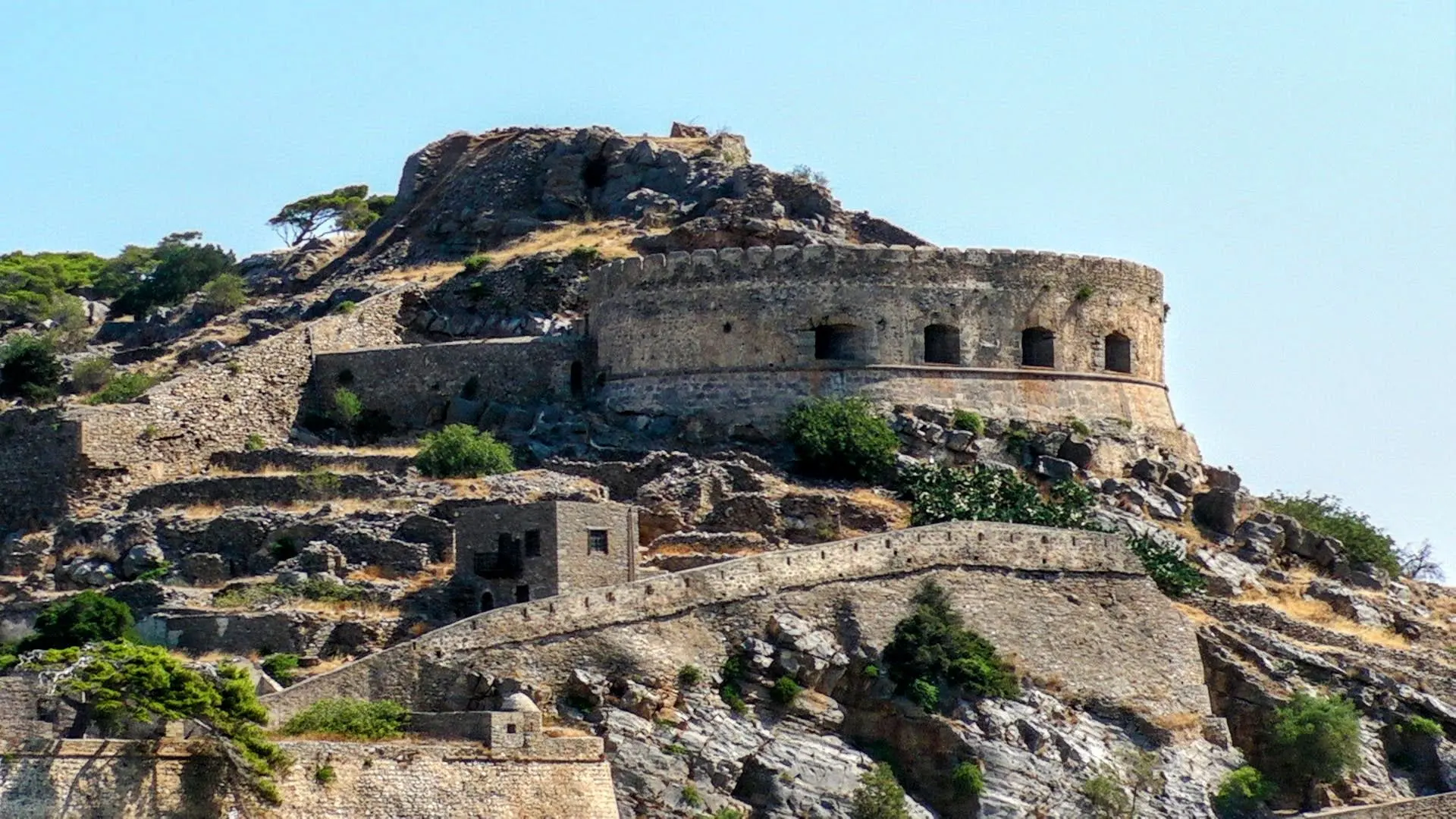 Spinalonga’s fortifications and settlement buildings rising above the shoreline.